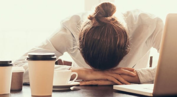 Woman-with-her-head-down-on-her-desk-and-several-coffee-cups